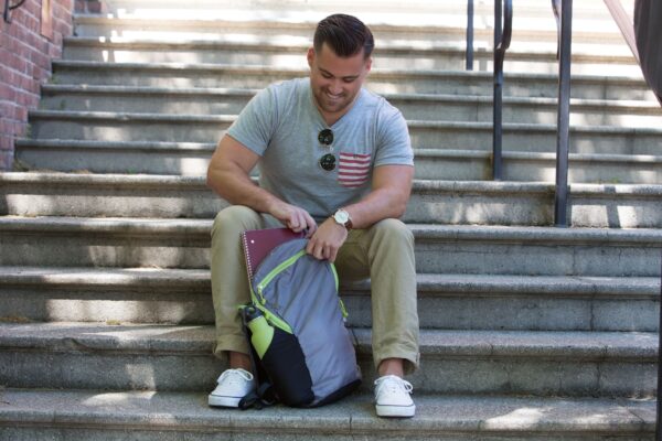 An individual sitting on cement stairs putting away a notebook into their eco friendly Chico Bag brand recycled plastics collapsible travel pack.