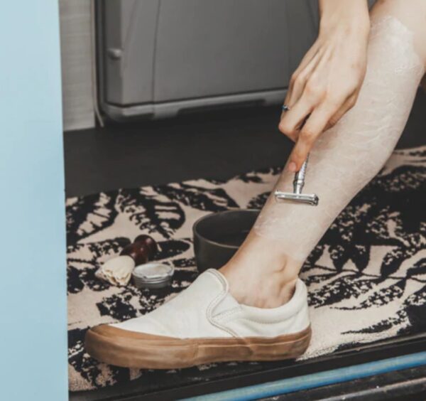 Woman traveler shaving legs in camping van with eco-friendly, plastic-free metal safety razor