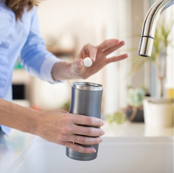 Woman holding bottle bright cleaning tablet over water bottle for sustainable cleaning