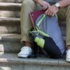 Zoomed in shot of an individual sitting on cement stairs putting away a notebook into their eco friendly Chico Bag brand recycled plastics collapsible travel pack.