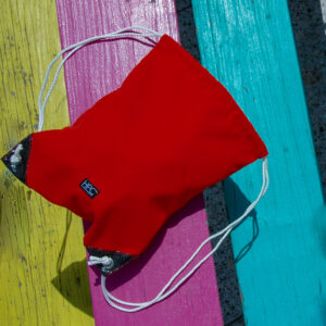 Hamilton Perkins brand recycled plastic red drawstring bag resting on a colorful picnic table.