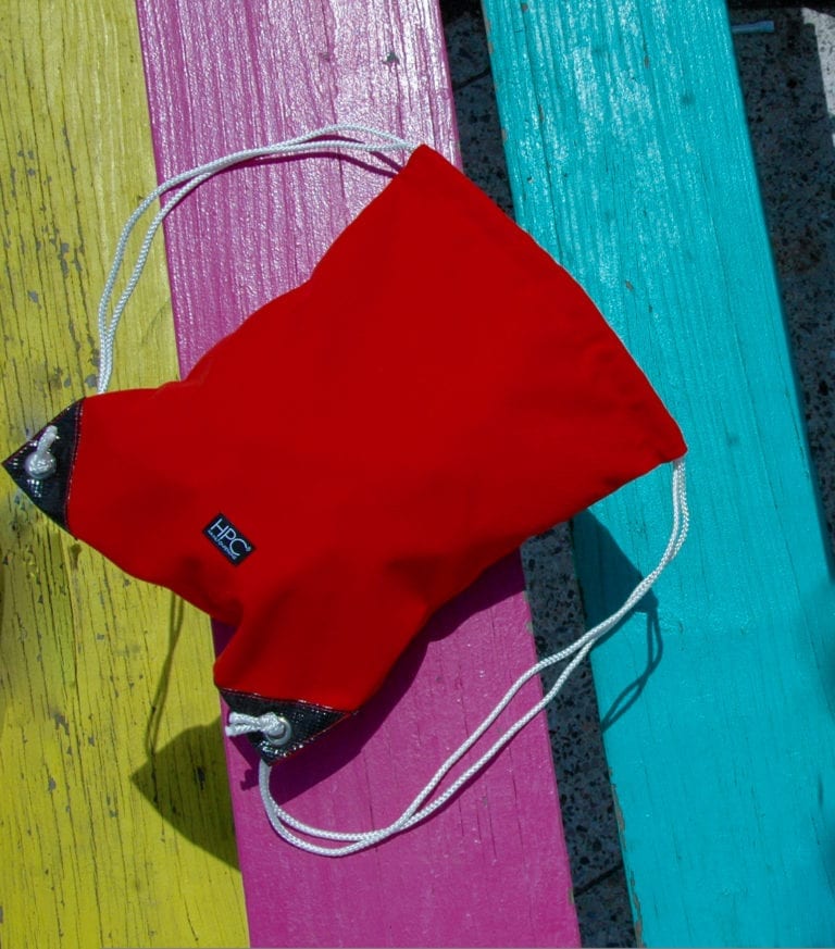 Hamilton Perkins brand recycled plastic red drawstring bag resting on a colorful picnic table.
