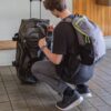 Individual squatting down next to suitcase wearing an eco friendly recycled plastics collapsible travel pack on his back.