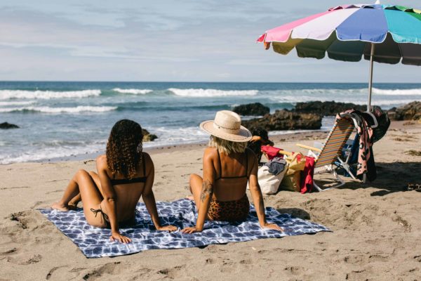 Woman at beach sitting on Nomadix Agua Blue festival blanket for sustainable travel