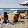 Woman at beach sitting on Nomadix Agua Blue festival blanket for sustainable travel