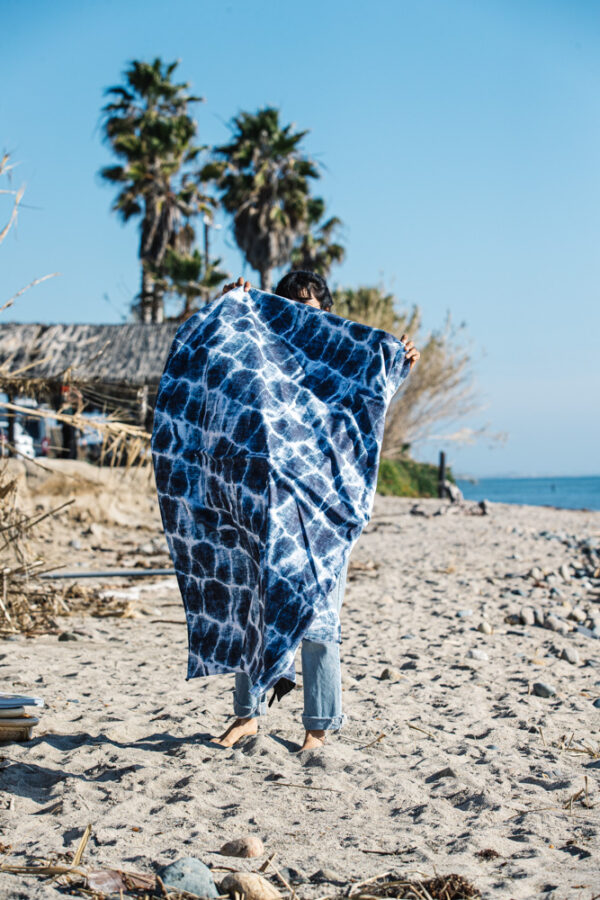 Person at beach unfolding Agua Blue eco-friendly, recycled festival blanket