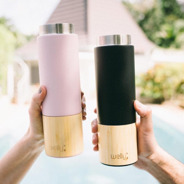 Rose and black eco friendly Welly brand 18 ounce bamboo and stainless insulated traveler bottles without loop caps held in the hands of two people.