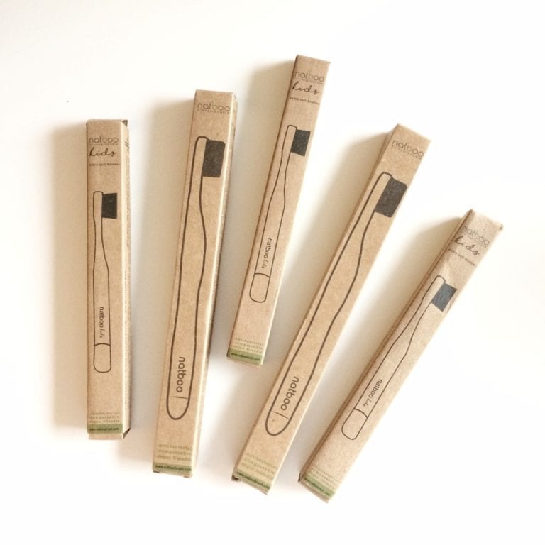 Overhead view of five earth friendly Natboo brand biodegradable bamboo toothbrush, in both adult and kid sizes, displayed in recycled packaging in alternating size pattern.