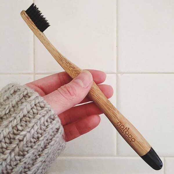 Pictured holding in hand an earth friendly Natboo brand biodegradable bamboo toothbrush with black tip.