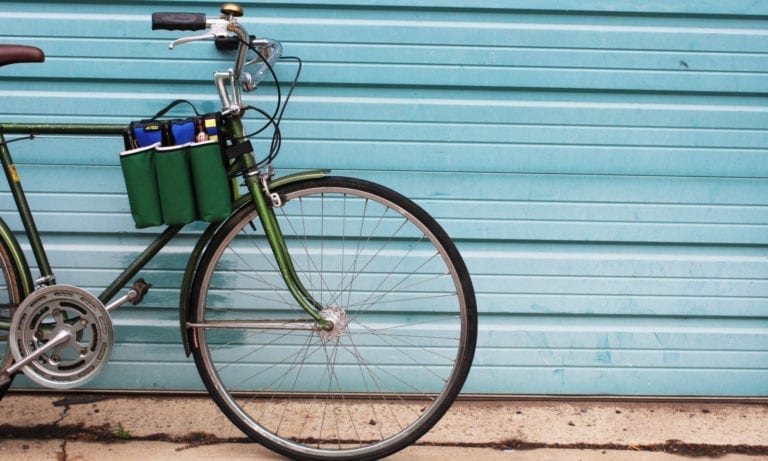 Side display of eco friendly Green Guru Gear brand Sixer 6-pack Top Tube Holder, loaded up with bottle brews, mounted on dark green bike.  Product is made from upcycled bicycle inner tubes, repurposed nylon fabric, and 18oz vinyl waterproof tarp.