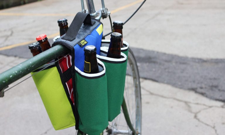 Point of view riding display of eco friendly Green Guru Gear brand Sixer 6-pack Top Tube Holder, loaded up with bottle brews, mounted on bike frame.  Product is made from upcycled bicycle inner tubes, repurposed nylon fabric, and 18oz vinyl waterproof tarp.