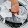 Adding a laundry filled sustainable Guppyfriend brand anti-microplastic laundry bag into a white washing machine to collect plastic fibers.