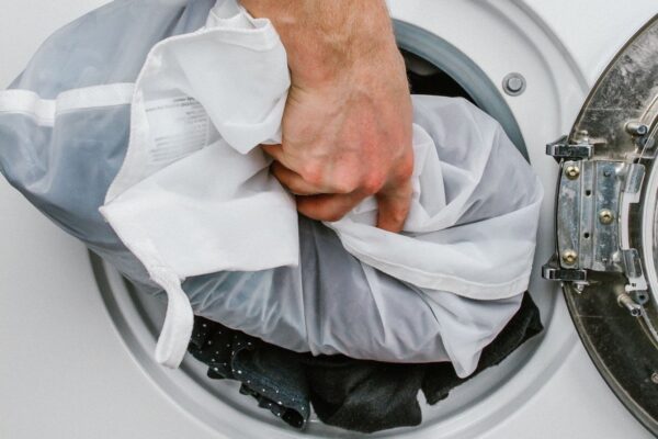 Adding a laundry filled sustainable Guppyfriend brand anti-microplastic laundry bag into a white washing machine to collect plastic fibers.