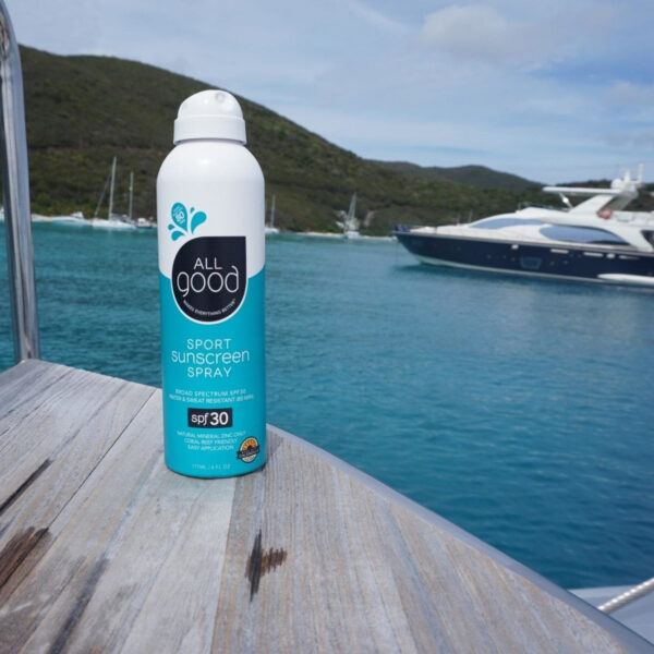 Sustainably made All Good Products brand reef friendly 30 SPF Sport Sunscreen Spray displayed on edge of wooden boat dock looking out into harbor of large boats.