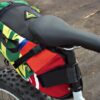 Multicolor upcycled fabric Green Guru Gear brand Haluer Seat Bag Bike Pack displayed on dirt trail mounted on white fat-tire bike with black seat.