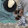 Hilana brand ultra soft navy blue and green and blue striped eco friendly Fethiye towels sprawled out on the beach with sandals and a sun hat.