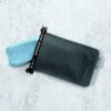 Environmentally friendly all black Matador brand FlatPak leak proof travel soap bar case with light blue bar of soap pictured partially inside case on white marble counter.