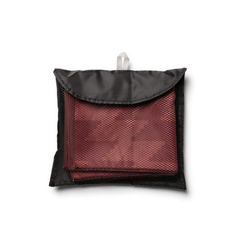 Product display of sustainable Nomadix brand, Mojave Red pattern, recycled ultralight compact travel towel folded up in small black mesh travel bag.
