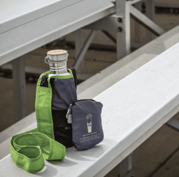 Recycled plastics Chico Bag brand bottle sling bag displayed on bleachers holding a stainless steel bottle and a folded up bottle sling bag leaning against the bottle sling bag holding the stainless steel bottle.