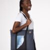 Model wearing Ten Tree brand daily tote bag in dark blue with a waves print; made with REPREVE fabric and BLOOM foam padding