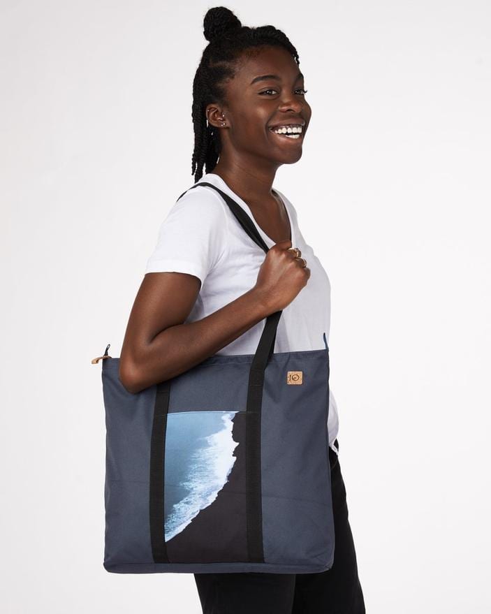 Model wearing Ten Tree brand daily tote bag in dark blue with a waves print; made with REPREVE fabric and BLOOM foam padding