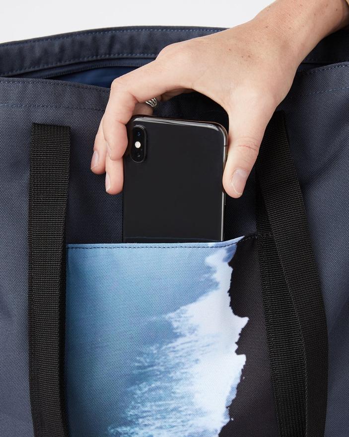 Close-up of the front of the daily tote bag, showing person placing a cell phone in the front pocket