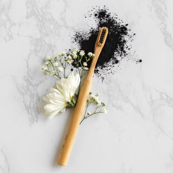 The Dirt brand eco friendly Bamboo Toothbrush with charcoal infused bristles displayed on white marble and surrounded by flowers.