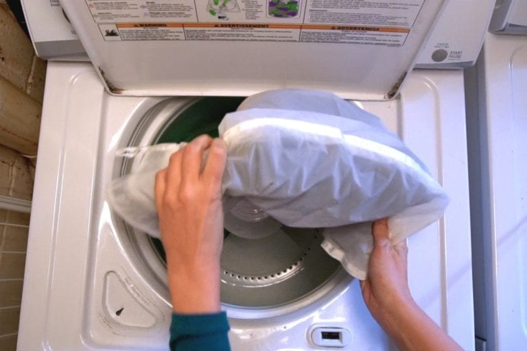 Filling up a white top load washing machine with eco friendly Guppyfriend brand anti-micro plastic laundry bag.