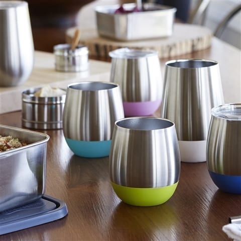 Eco friendly U-Konserve brand insulated stainless tumblers in all different colors and sizes spread across wooden table top.