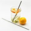 U-Konserve brand sustainable straw cleaning brush laying in front of a Ball mason jar filled with lemon water, a reusable stainless straw, and a full lemon sitting next to the glass.