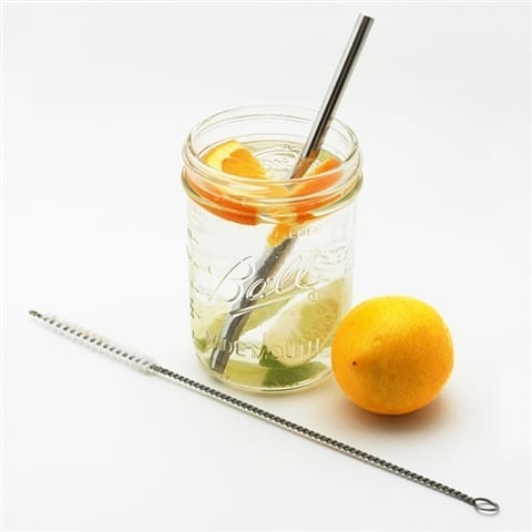 U-Konserve brand sustainable straw cleaning brush laying in front of a Ball mason jar filled with lemon water, a reusable stainless straw, and a full lemon sitting next to the glass.