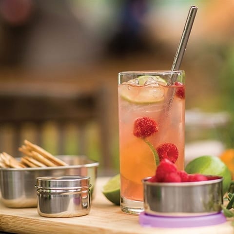 Fruity drink with stainless steel straw in glass surrounded by table top covered in appetizers served in eco friendly reusable tin containers and trays.  Stainless steel straw made by earth friendly U-Konserve brand.
