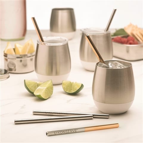 Eco friendly U-Konserve brand insulated stainless tumblers with stainless steel mini copper color straws used to sip with. Displayed on dinning table with fresh cut limes and a fruit platter served on reusable tin containers.  Straws sold in four pack.
