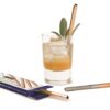 Sustainable U-Konserve brand stainless steel mini copper color straw used to sip cocktail with. Displayed with four pack of straws spread around drink.