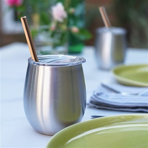 Eco friendly U-Konserve brand insulated stainless tumbler with stainless steel mini copper color straw used to sip with. Displayed on dinning table with plates set.  Straws sold in four pack.