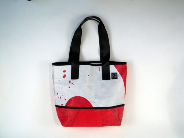 Large tote bag made of upcycled advertising banners from Alchemy Goods; shown with red and white print