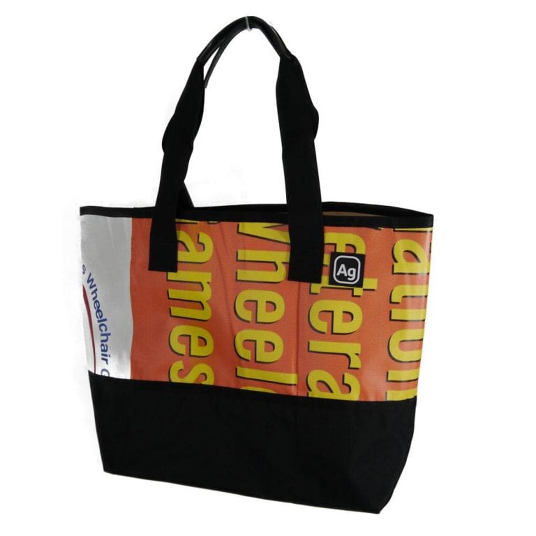Large tote bag made of upcycled advertising banners from Alchemy Goods; shown with yellow and orange print