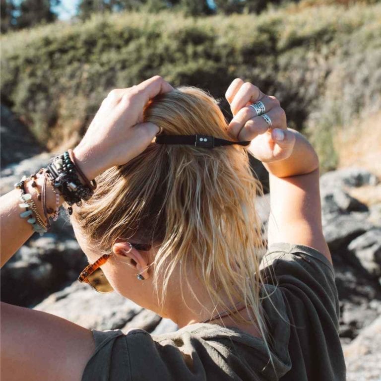 Female with long blonde hair using a black colored eco friendly Kooshoo brand plastic-free organic hair tie to hold up ponytail.