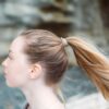 Female with long blonde hair using a gray colored eco friendly Kooshoo brand plastic-free organic hair tie to hold up ponytail.