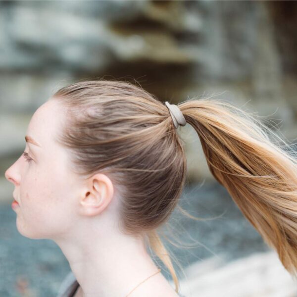 Female with long blonde hair using a gray colored eco friendly Kooshoo brand plastic-free organic hair tie to hold up ponytail.