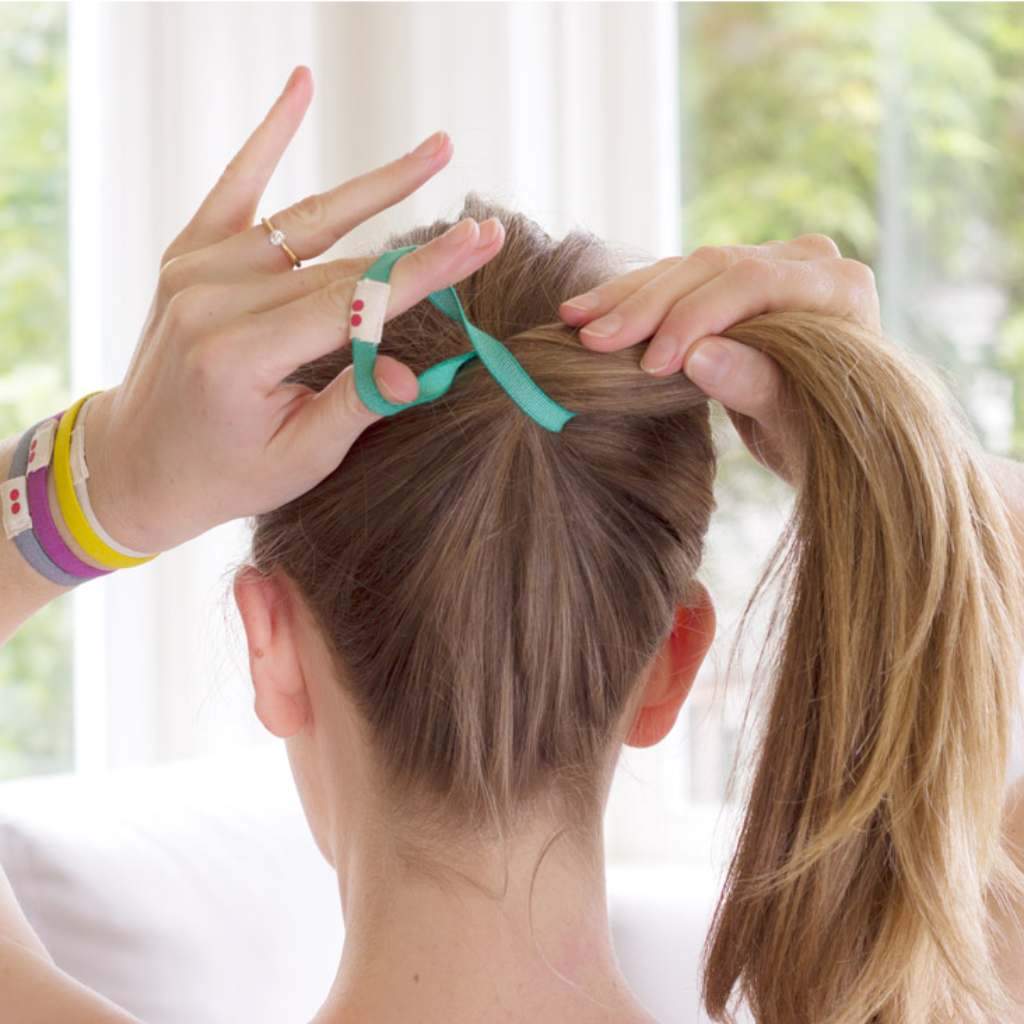 Female with long blonde hair using a green colored eco friendly Kooshoo brand plastic-free organic hair tie to hold up ponytail.