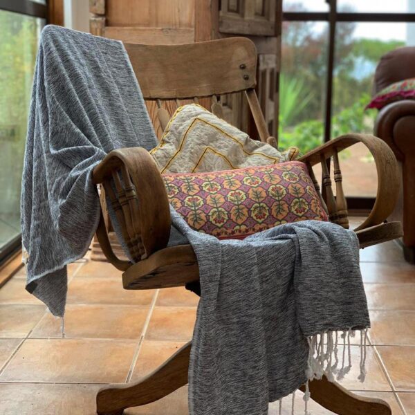 Hilana brand ultra-soft, earth friendly black Yalova blanket/throw displayed next to two pillows on a rustic wooden office chair.