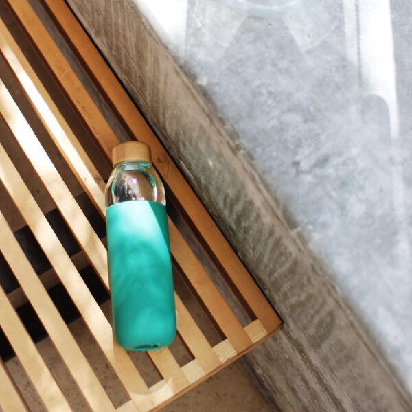 Sustainable Soma brand glass water bottle with emerald green silicone sleeve resting on bench.