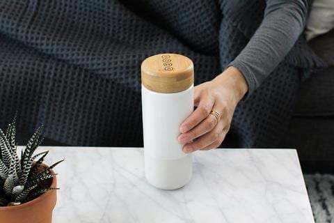 Soma brand eco friendly pearl white insulated ceramic travel mug with bamboo cap in hand displayed on white quartz counter top.