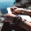 Person writing outside wearing multiple bracelets and a sustainable Kooshoo brand black plastic-free organic hair tie on their wrist.