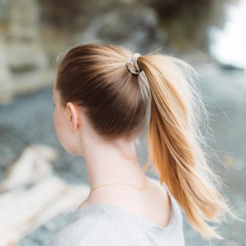 Female with long blonde hair using a natural colored eco friendly Kooshoo brand plastic-free organic hair tie to hold up ponytail.