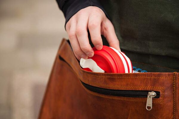 Earth friendly Pokito brand red and white pocket sized cup collapsed to pocket size and placing into leather bag.