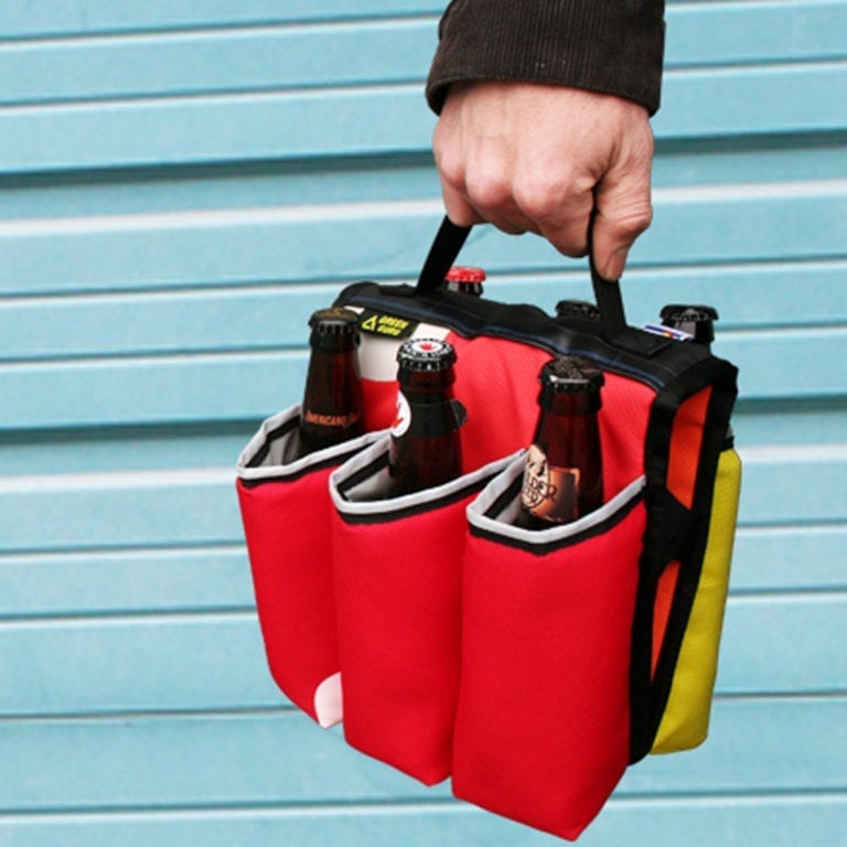 Carrying Eco friendly Green Guru Gear brand Sixer 6-pack Top Tube Holder, by black handle, loaded up with bottle brews. Product is made from upcycled bicycle inner tubes, repurposed nylon fabric, and 18oz vinyl waterproof tarp.   Pictured is a red, black, and white color pattern with black handle.
