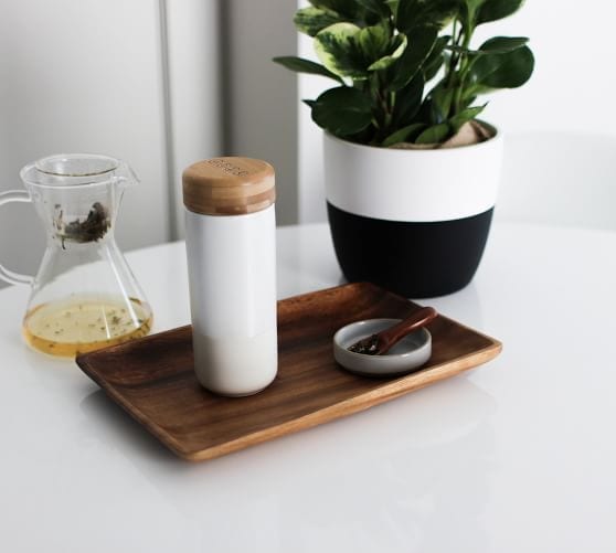 Soma brand eco friendly pearl white insulated ceramic travel mug with bamboo cap displayed on white counter top with loose leaf tea.
