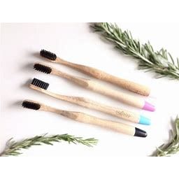 Four earth friendly Natboo brand biodegradable round bamboo toothbrush with white and black tip pictured side by side with green floral decor surrounding them.